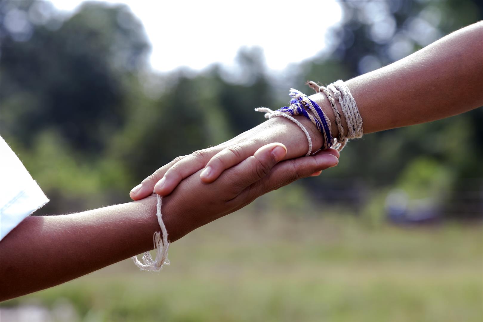 two hands holding, wearing cultural strings on their wrists