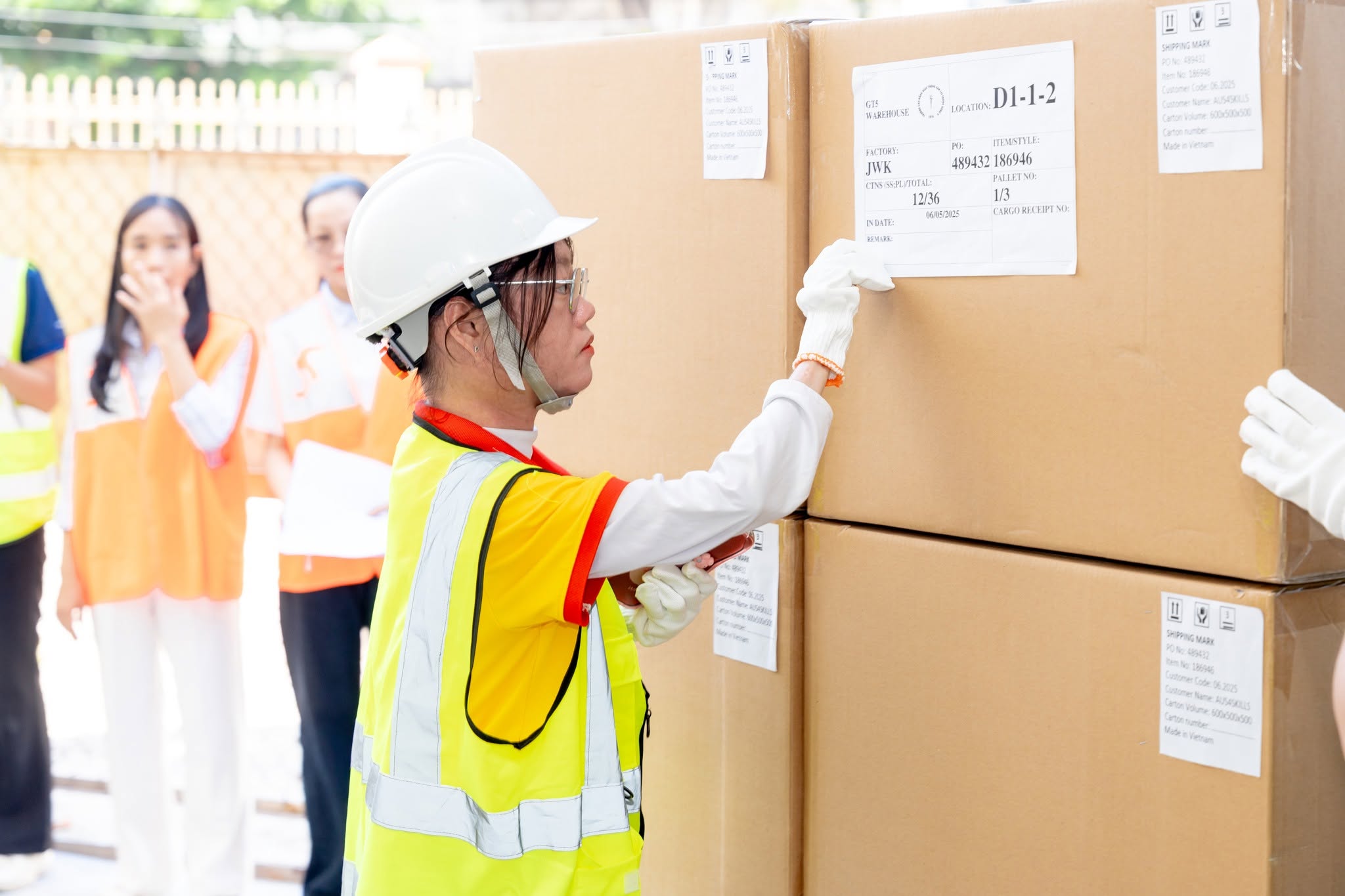 Logistics VET student wearing a hard hat and high viz vest, sticking a label on a box in a warehouse